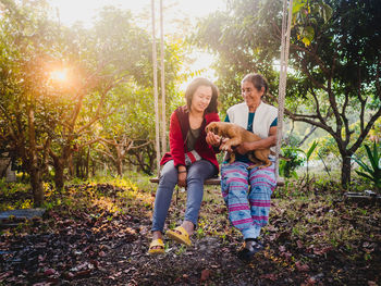 Mother and daughter with dog on swing at park during sunset