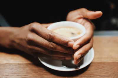 Close-up of hand holding coffee cup on table