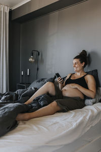 Happy pregnant woman relaxing in bed and using phone