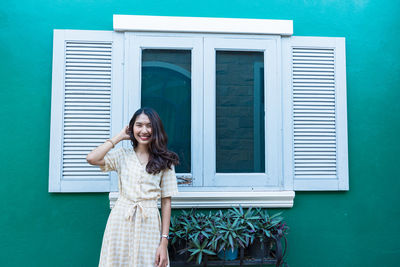 Portrait of a smiling young woman standing against blue door