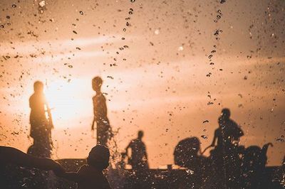 Silhouette people on wet glass against sky during sunset