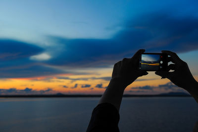 Man photographing through smart phone against sky during sunset