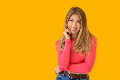 Portrait of young woman standing against yellow background