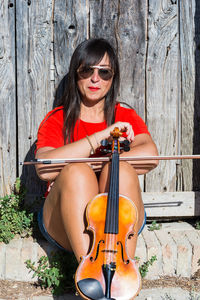 Close-up of woman with violin sitting against wall