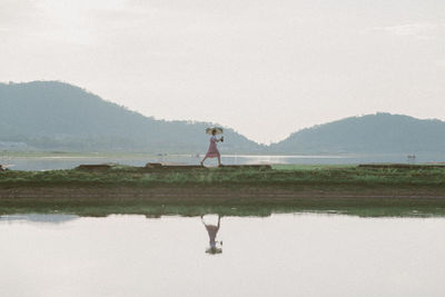 Woman standing by lake against sky