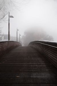 Empty footpath by railing against sky during winter