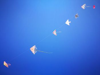 Low angle view of kites against clear blue sky