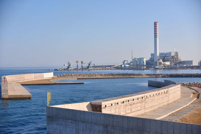 View of factory by sea against clear sky