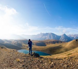 Mid adult man photographing while standing on mountain against blue sky