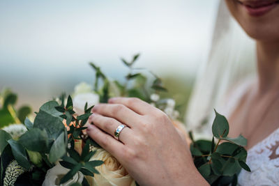 Wedding ring on bride hand detail with wedding bouquet of flowers