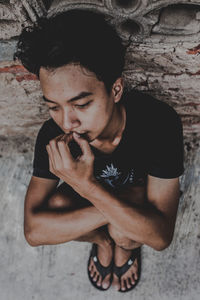 Young man looking away while sitting on wall