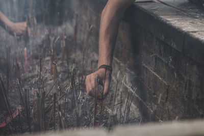 Cropped hand of man placing lit incense stick in ash