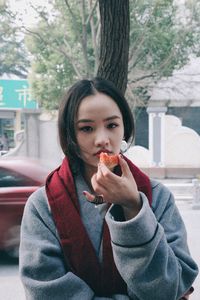 Portrait of young woman eating food on tree trunk