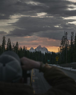 Person on road by trees against sky during sunset