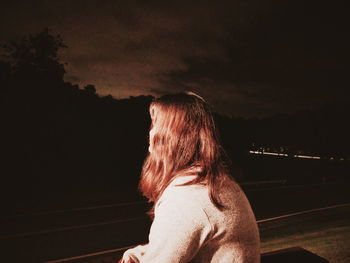 Rear view of woman looking down against sky at night