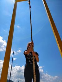 Low angle view of girl standing holding rope against sky