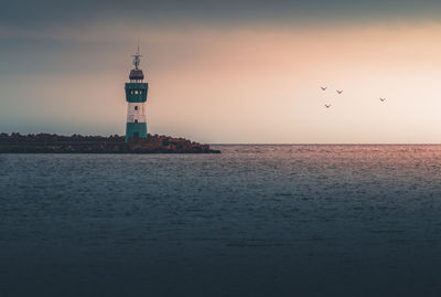 Lighthouse by sea against sky during sunset