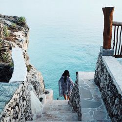 High angle rear view of woman moving down from steps towards sea