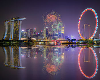 Firework display by lake and marina bay sands in city at night