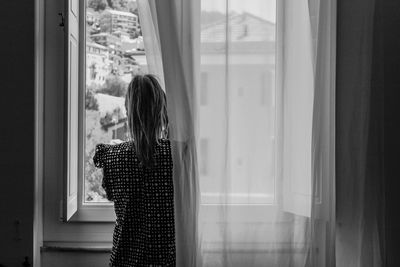 Rear view of woman standing by window at home