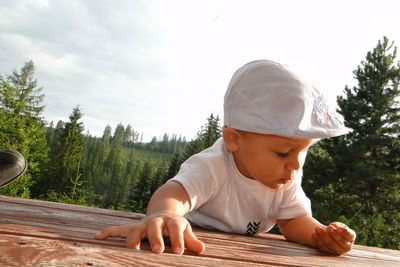 Close-up of boy leaning on wooden table against forest