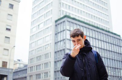 Portrait of young man gesturing against buildings in city