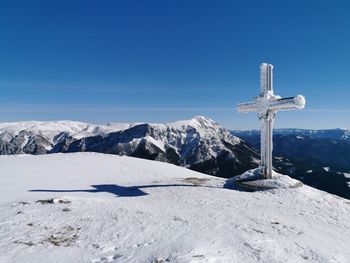 Cross on snowcapped mountain against blue sky