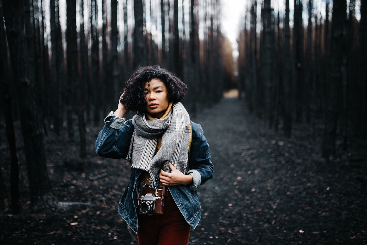 forest, one person, tree, land, woodland, standing, nature, casual clothing, young adult, front view, trunk, plant, three quarter length, tree trunk, clothing, hair, looking, day, hairstyle, outdoors