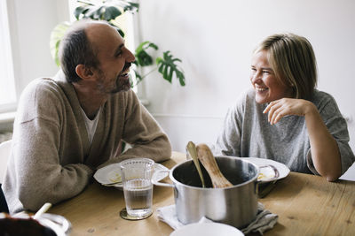 Happy mature couple talking to each other sitting at dining table in home