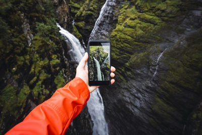 Person taking smartphone picture of a waterfall, lapland, norway