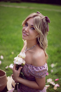 Portrait of a beautiful young woman sitting on a green meadow in summer and holding a bouquet 