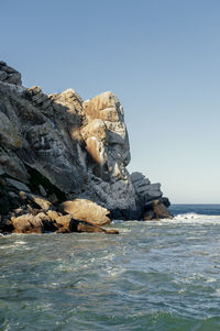 Rock formation in sea against clear blue sky