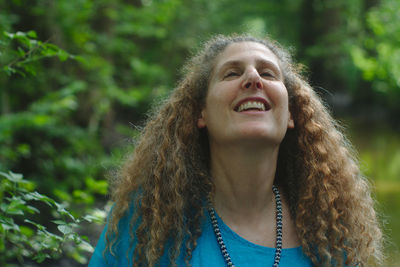 Smiling woman with curly hair standing at forest