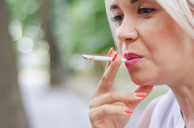 Woman smokes cigarette. holds in mouth, red lips