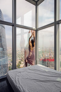 Woman in a nightgown stands at the window in a skyscraper near the bed