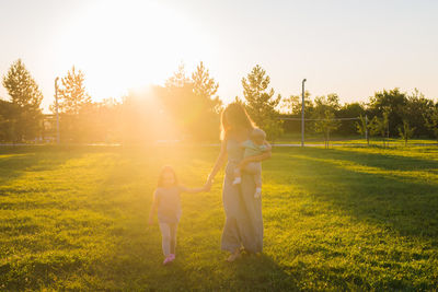 Rear view of women standing on grass against trees