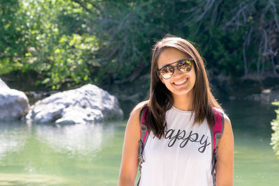 Close-up of smiling young woman standing by lake