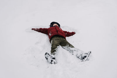 Best outdoor winter activities for kids. happy kid boy in red winter jacket making snow angel
