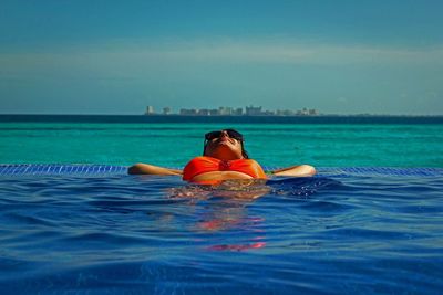 Young woman resting in infinity pool against sky