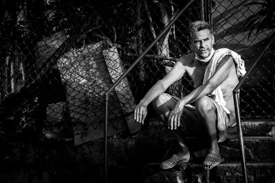 Portrait of young man sitting by chainlink fence