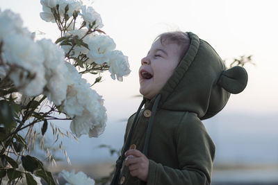 Cheerful toddler girl smelling white roses in the rose garden