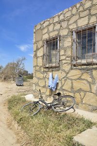 Bicycle by building on field against sky