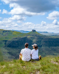 Rear view of woman sitting on mountain against sky