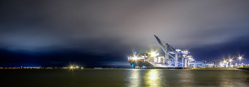 Panoramic shot of sea by illuminated dock against sky at night