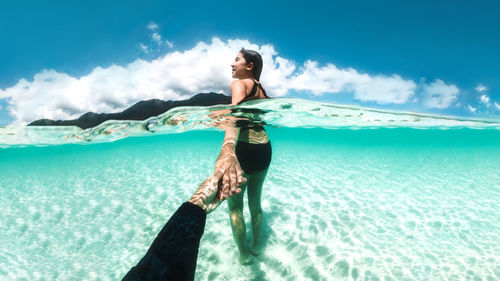 Young woman holding hands while standing in sea against sky