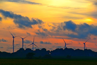 Silhouette wind turbines on field against sky during sunset