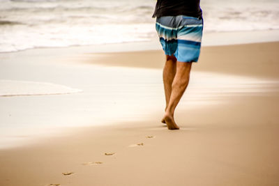 Low section of man walking on beach