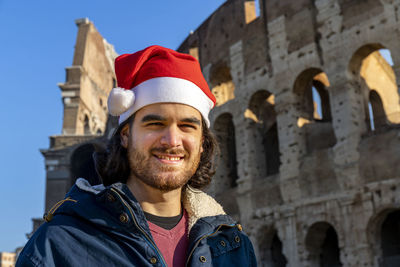 Beautiful man traveling to rome. the young man wears santa's hat and smiles at the camera.