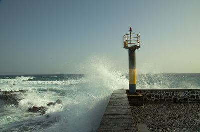 Waves splashing on retaining wall against clear blue sky