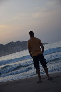 Rear view of man standing on beach during sunset